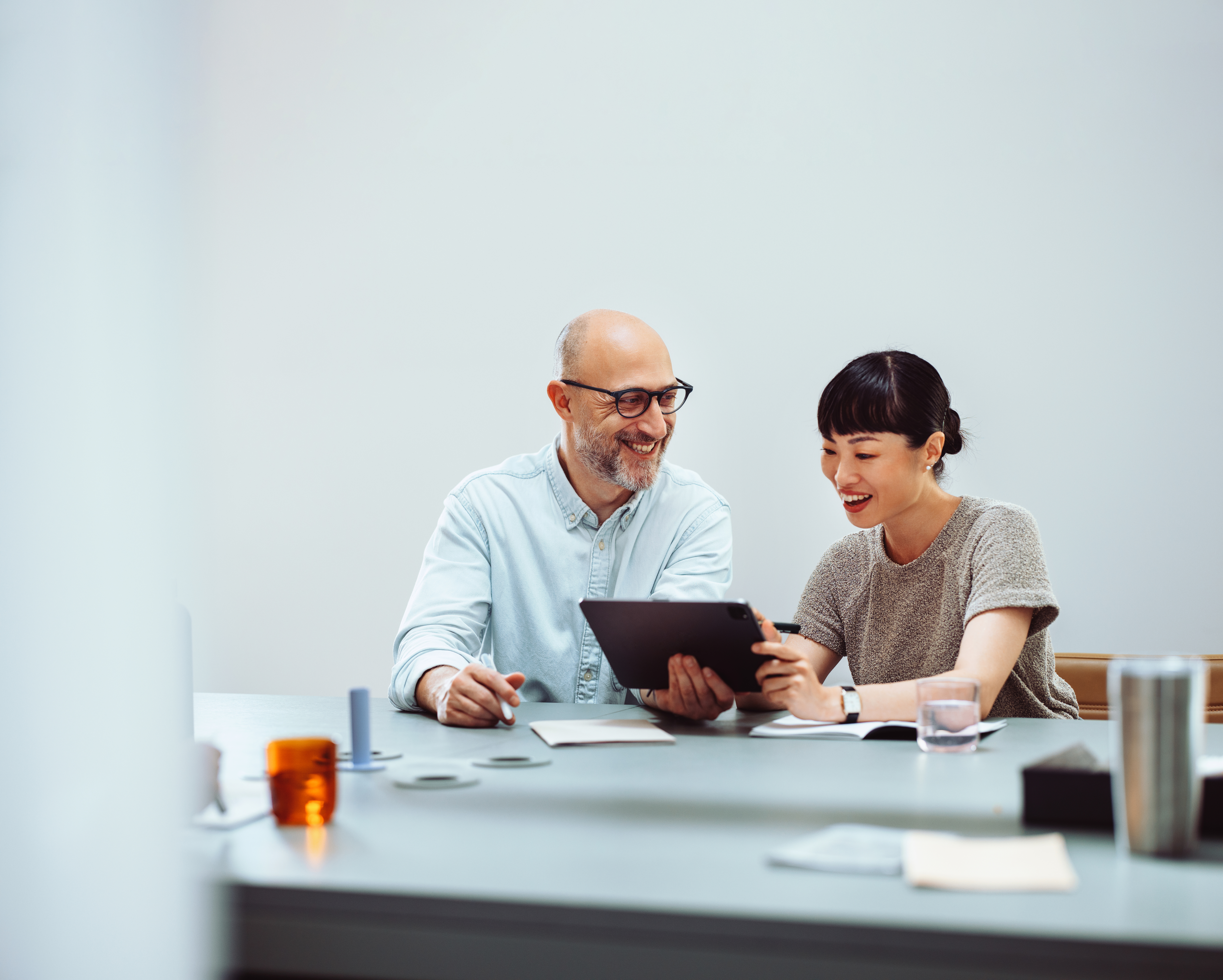 Businessman and businesswoman happily collaborating on a project using a digital tablet in a modern office setting.