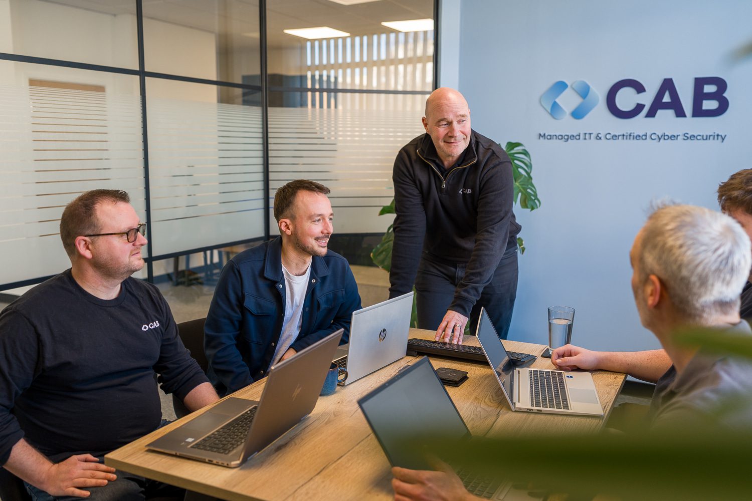 CAB IT team gathered around their laptops smiling in the meeting room