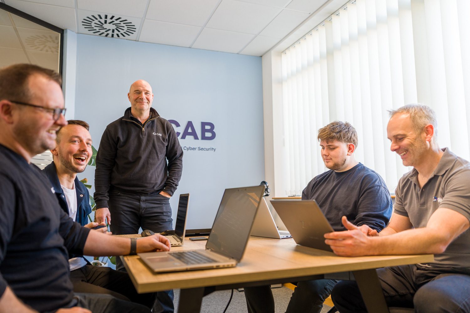 CAB IT team gathered around their laptops smiling in the meeting room